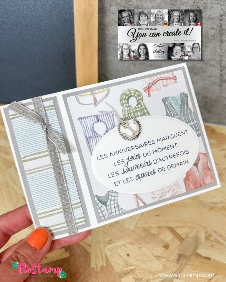 Eine Hand hält eine verzierte Geburtstagskarte mit französischem Text, die mit Pastellmustern, einer Schleife und einem kleinen Anhänger verziert ist. Im Hintergrund ist ein Flyer mit der Aufschrift „Mach war draus Juli 26“ zu sehen, der der Szene eine kreative Note verleiht.
