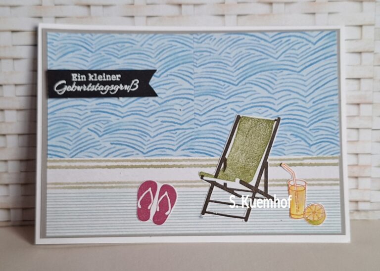 Eine Karte mit einer Strandszene, einem Liegestuhl, Flip-Flops und einem Getränk. Auf einem Banner steht auf Deutsch „Ein kleiner Geburtstagsgruß“. Das fröhliche Motiv eignet sich perfekt, um den 26. Juli auf sonnige Art zu feiern.