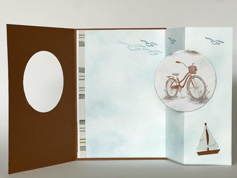 Eine handgefertigte Karte mit braunem Umschlag, auf dem ein Fahrrad und ein Segelboot abgebildet sind, sowie blaue Vögel am Himmel vor einem hellen Hintergrund – ideal, um die Kreativität anzuregen oder als Teil Ihres Projekts „Mach was draus – 26. Juli“.