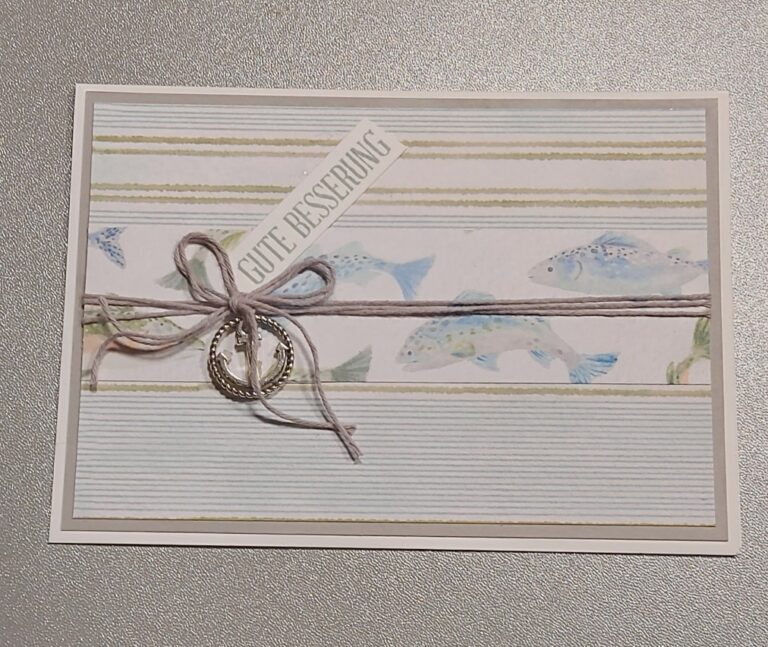 Grußkarte mit pastellfarbenem Fischmotiv, einer zu einer Schleife gebundenen Schnur mit einem kleinen Anker-Anhänger und einem Etikett mit der Aufschrift „GUTE BESSERUNG“ auf gestreiftem Hintergrund – eine schöne Inspiration von „Mach was draus“ vom 26. Juli.