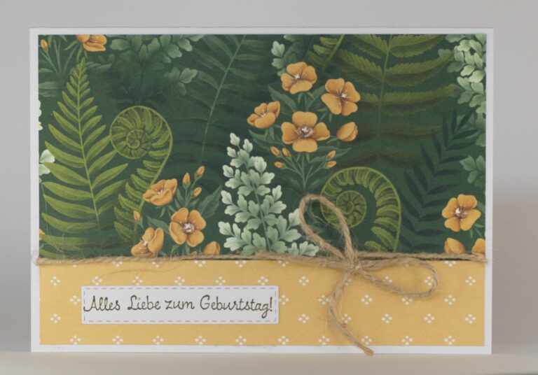 Eine Geburtstagskarte mit Blumen- und Farnmotiv, gelben Blumen, einer Schleife aus Bindfaden und einem deutschen Geburtstagsgruß: „Alles Liebe zum Geburtstag!“ – perfekt, um jemandem Besonderen am 26. August eine Überraschung zu bereiten.