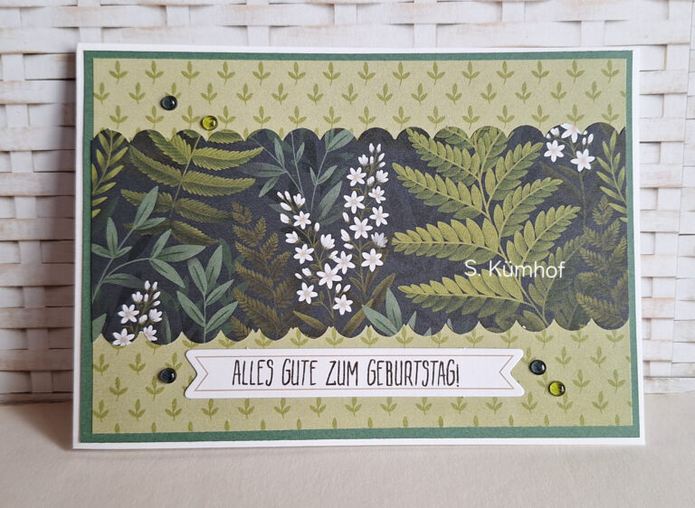 Eine handgefertigte Karte mit einem Blatt- und Blumenmotiv, verziert mit Pailletten und dem deutschen Text „Alles Gute zum Geburtstag!“ auf einem weißen Band – eine wunderschöne Kreation, inspiriert von „Mach was draus“ vom 26. August.