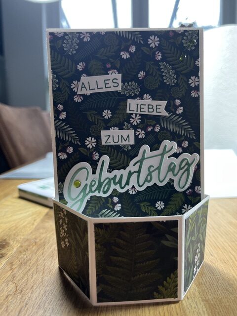 Eine Pop-up-Karte mit Blumenhintergrund zeigt den deutschen Schriftzug „Alles Liebe zum Geburtstag“ auf einem Holztisch am Fenster; sie entstand im Rahmen der „Mach was draus“-Challenge vom 26. August.