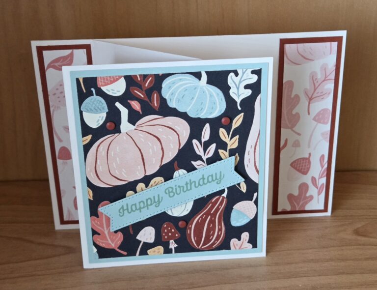 Eine handgefertigte Geburtstagskarte mit Motiven rund um Kürbisse und den Herbst steht auf einer Holzunterlage – perfekt für „Mach was draus“ am 26. September – und trägt auf der Vorderseite die Aufschrift „Happy Birthday“.
